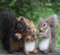 three stuffed squirrels are standing next to each other on a wooden surface with trees in the background