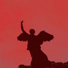 the silhouette of an angel with outstretched arms against a red sky background, in front of a black statue