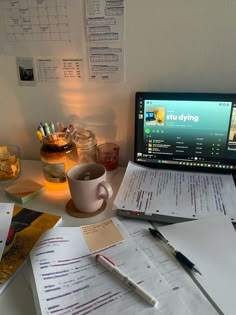 a laptop computer sitting on top of a desk next to papers and cups filled with pens