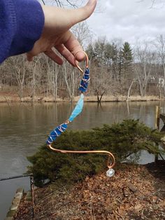 a person is holding an object in their hand next to the water and some trees