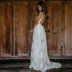 a woman standing in front of a wooden door wearing a white wedding dress with open back