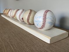 four baseballs are lined up on a wooden shelf next to a wall with a clock in the background