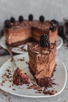 a piece of chocolate cake on a plate with a slice cut out and some blackberries