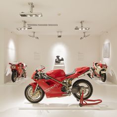 two red motorcycles are on display in a white room