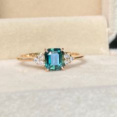 an emerald colored ring with three diamonds on the band and in a white velvet box