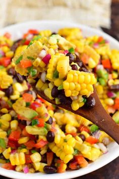 a wooden spoon filled with corn salad on top of a white plate next to a brown table