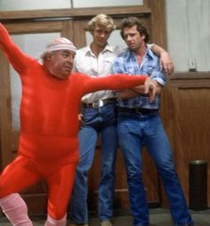 an old man in a red suit is dancing while two men look on from behind him