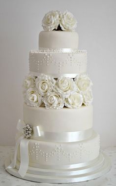 a three tiered wedding cake with white roses on top and ribbons around the edges