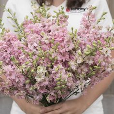 a woman holding a bunch of pink flowers in her hands and wearing a white t - shirt