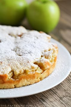 an apple pie on a white plate next to green apples