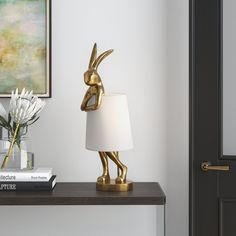 a gold rabbit lamp sitting on top of a table next to a white flower vase