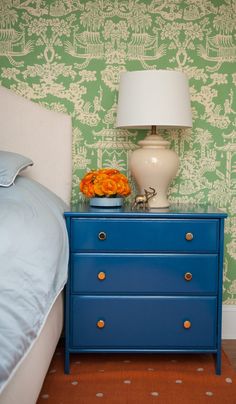 a blue dresser sitting next to a bed in a room with green wallpaper and a white lamp