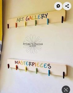 three wooden pegs are hanging on the wall with name tags attached to them, and there is a sign that says art gallery