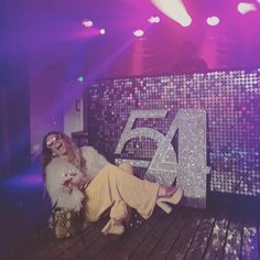 a woman sitting on top of a wooden floor next to a large number 54 sign