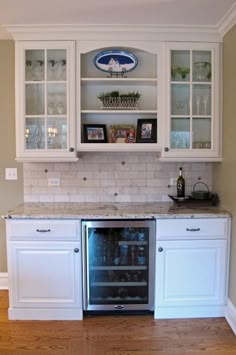 a kitchen with white cabinets and marble counter tops, an open wine cooler in the center