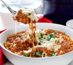 a spoon full of chili and cheese being lifted from a white bowl with pasta in it