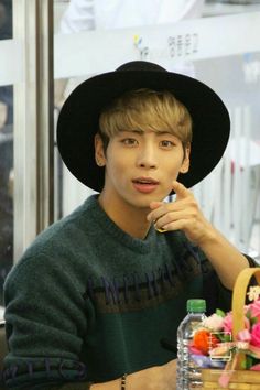 a young man wearing a black hat sitting at a table with flowers in front of him