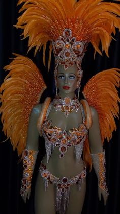 a woman in an orange costume with large feathers on her head and chest, standing next to a black curtain