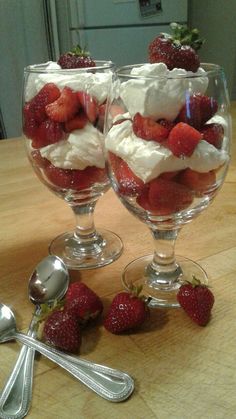 two glasses filled with strawberries on top of a wooden table next to spoons