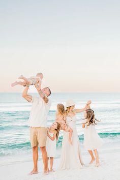 a family standing on the beach with their baby girl in her arms and dad holding him up