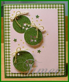 two green christmas ornaments on top of a pink card with gold stars and ribbon around them