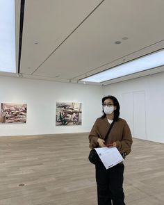 a woman wearing a mask and holding a clipboard in an empty room with paintings on the walls