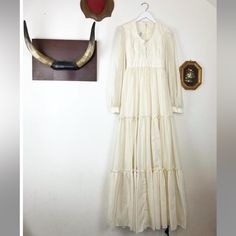 a white dress hanging on the wall next to an antler's head and hat