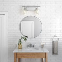 a bathroom with white brick walls and a round mirror above the sink, next to a wooden stool