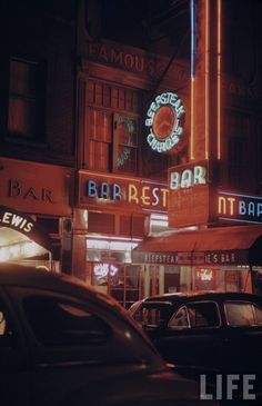 cars are parked in front of a bar and restaurant on a city street at night