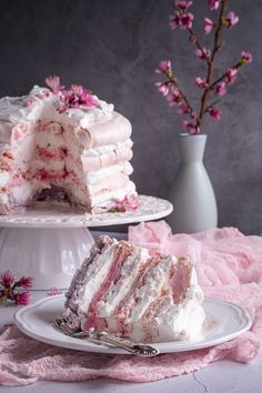 a piece of cake on a white plate with pink flowers and a vase in the background