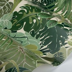 a green and white tropical print fabric with large leaves on the bottom half of it