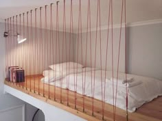 there is a bed with red strings hanging from the wall above it and books on the floor below