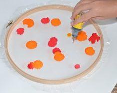 a person is painting an orange and red design on a piece of paper with glue