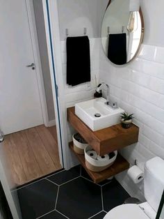 a white toilet sitting next to a sink in a bathroom under a round mirror on the wall