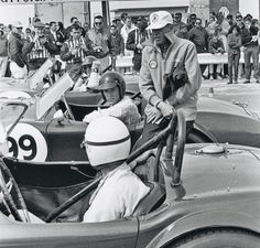 an old black and white photo of two men in a race car with people watching