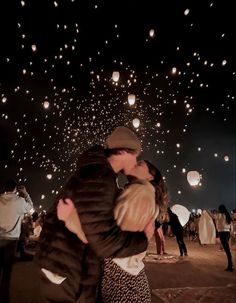 two people embracing each other in front of many lit up lanterns flying overhead at night