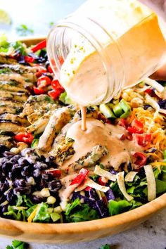 someone pouring dressing over a salad in a bowl