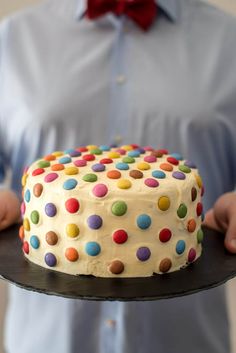 a man holding a cake with white frosting and multicolored polka dots on it