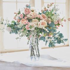 a vase filled with pink and white flowers on top of a table next to a window