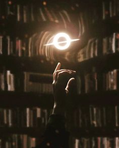 a person holding up a small object in front of a book shelf filled with books