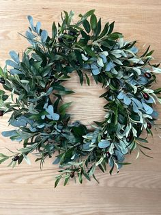 a wreath made out of green leaves and berries on a wooden surface with the center surrounded by greenery