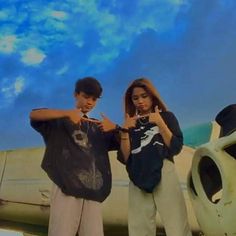 two people standing next to each other in front of an airplane with the sky behind them