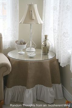 a table with a lamp on it next to a chair in front of a window