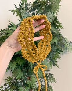 a hand holding up a crocheted piece of yarn next to a potted plant