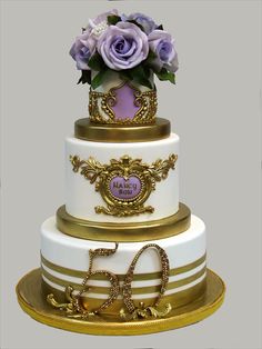 a three tiered wedding cake with purple flowers on top and gold trimmings