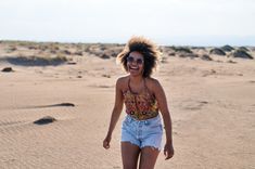 a woman walking across a sandy beach next to a blue frisbee in her hand