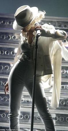 lady in black and white outfit on stage with microphone, hat and coat over her shoulders