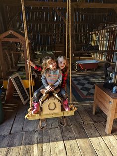 two young children sitting on a wooden swing