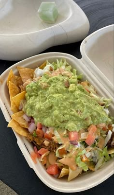 a white container filled with nachos and guacamole on top of a table