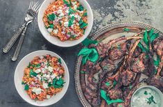 two bowls filled with food next to silverware and forks on a table top,